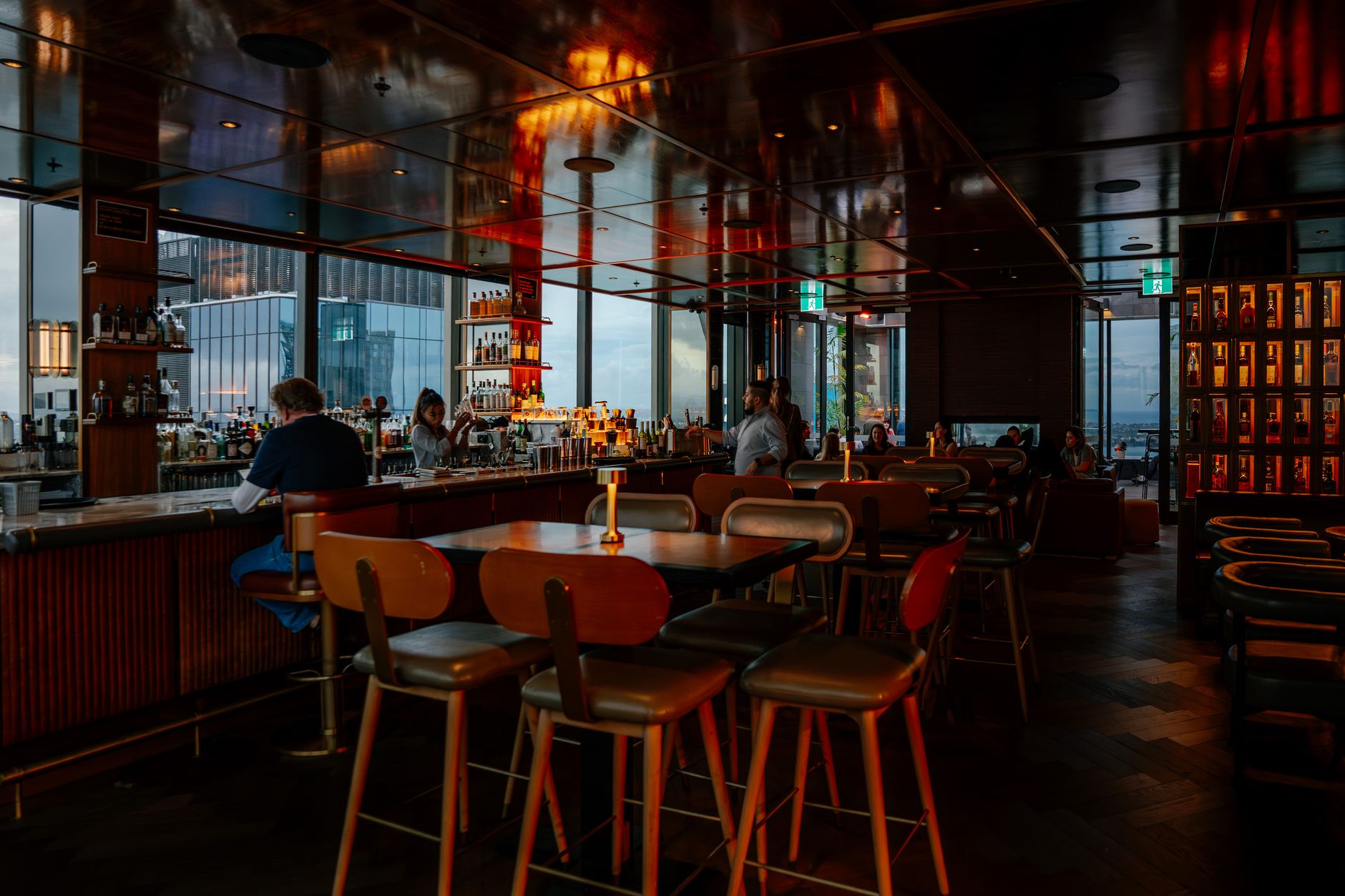 Warm, dimly lit rooftop bar lounge with guests over cocktails, the indoor sky-bar atmosphere of spots like Cloud 9 among the best rooftop bars in Shanghai