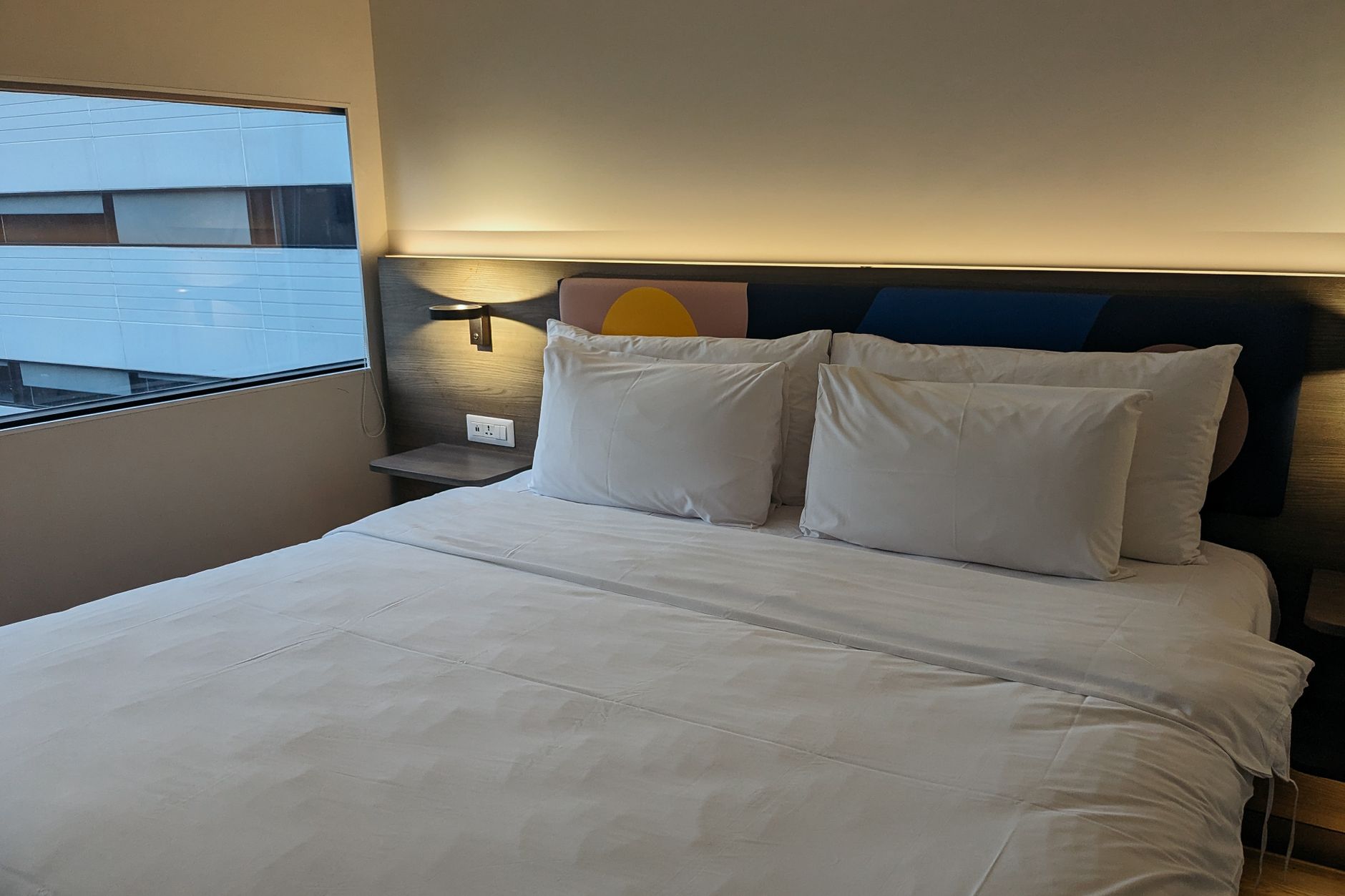 A simple modern hotel room with white linens and a city view, typical of the mid-range chains near Pudong Airport