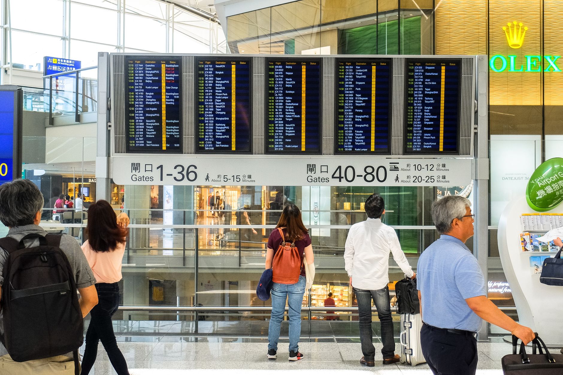 Passengers checking a departure information board in an airport terminal during a layover
