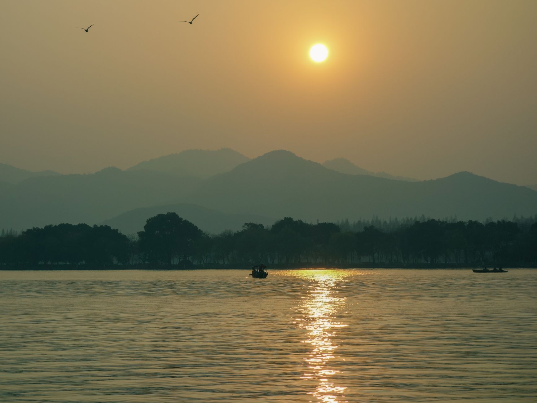 Boats on West Lake in Hangzhou at sunset with hills behind