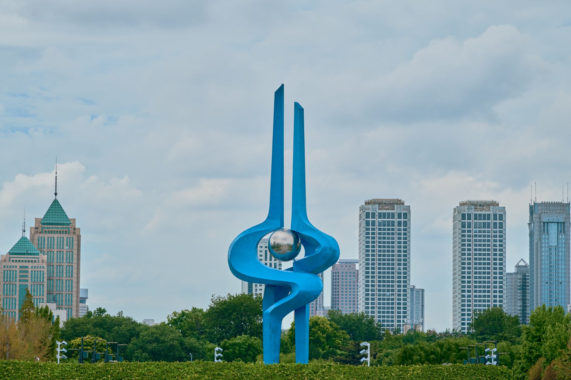 A modern abstract sculpture standing outdoors against a city skyline