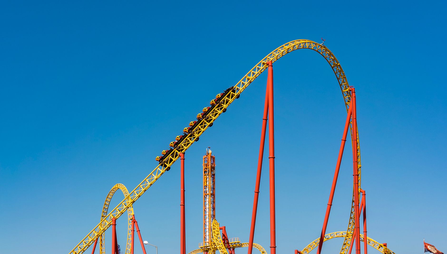 A steel roller coaster track curving against a clear blue sky at a theme park