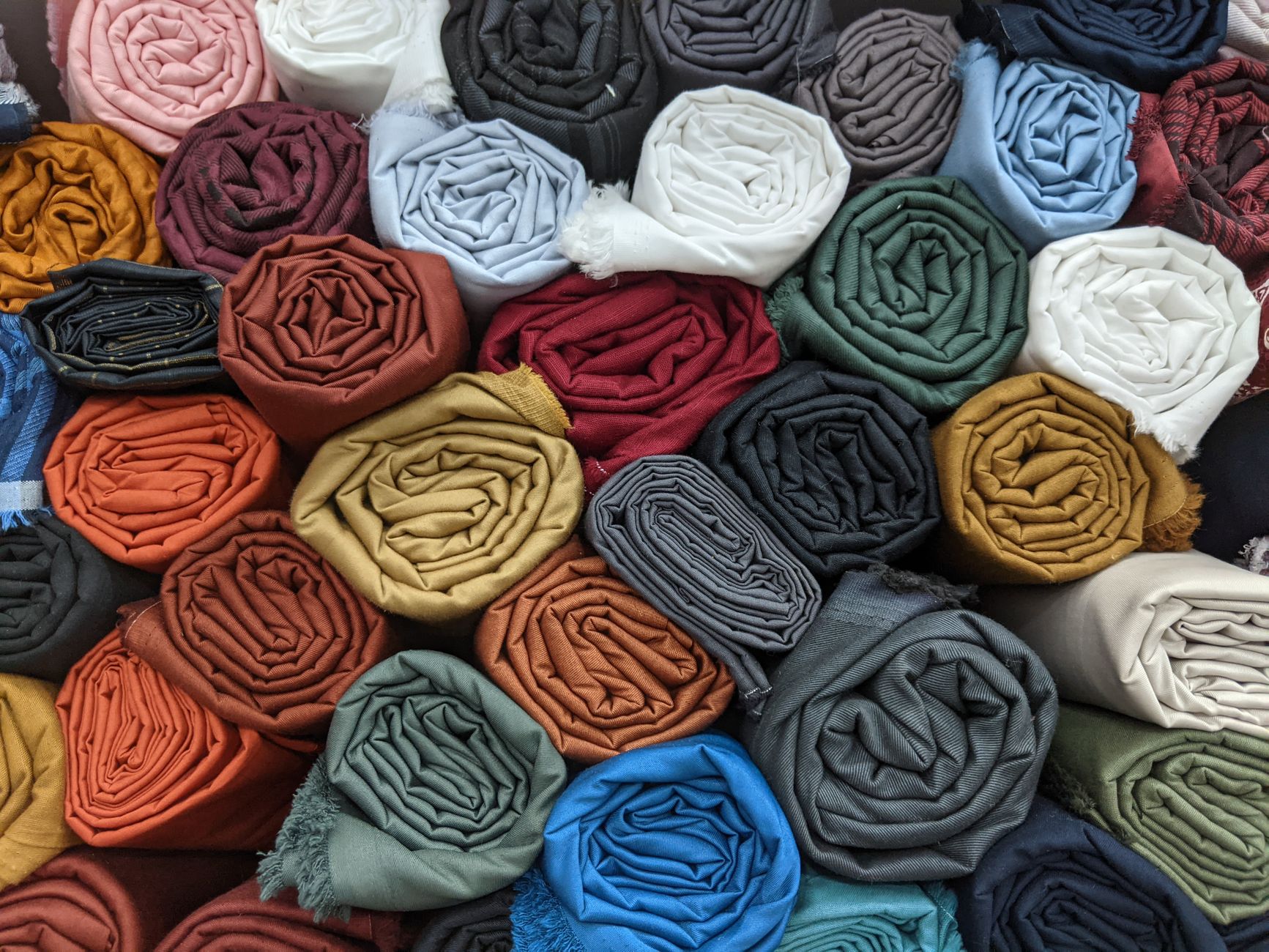 Rolls of fabric in many colours stacked on shelves at a textile market stall