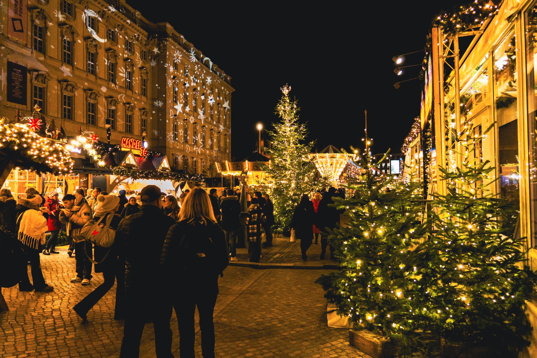 Illuminated wooden stalls and crowds at a Christmas market on a winter evening