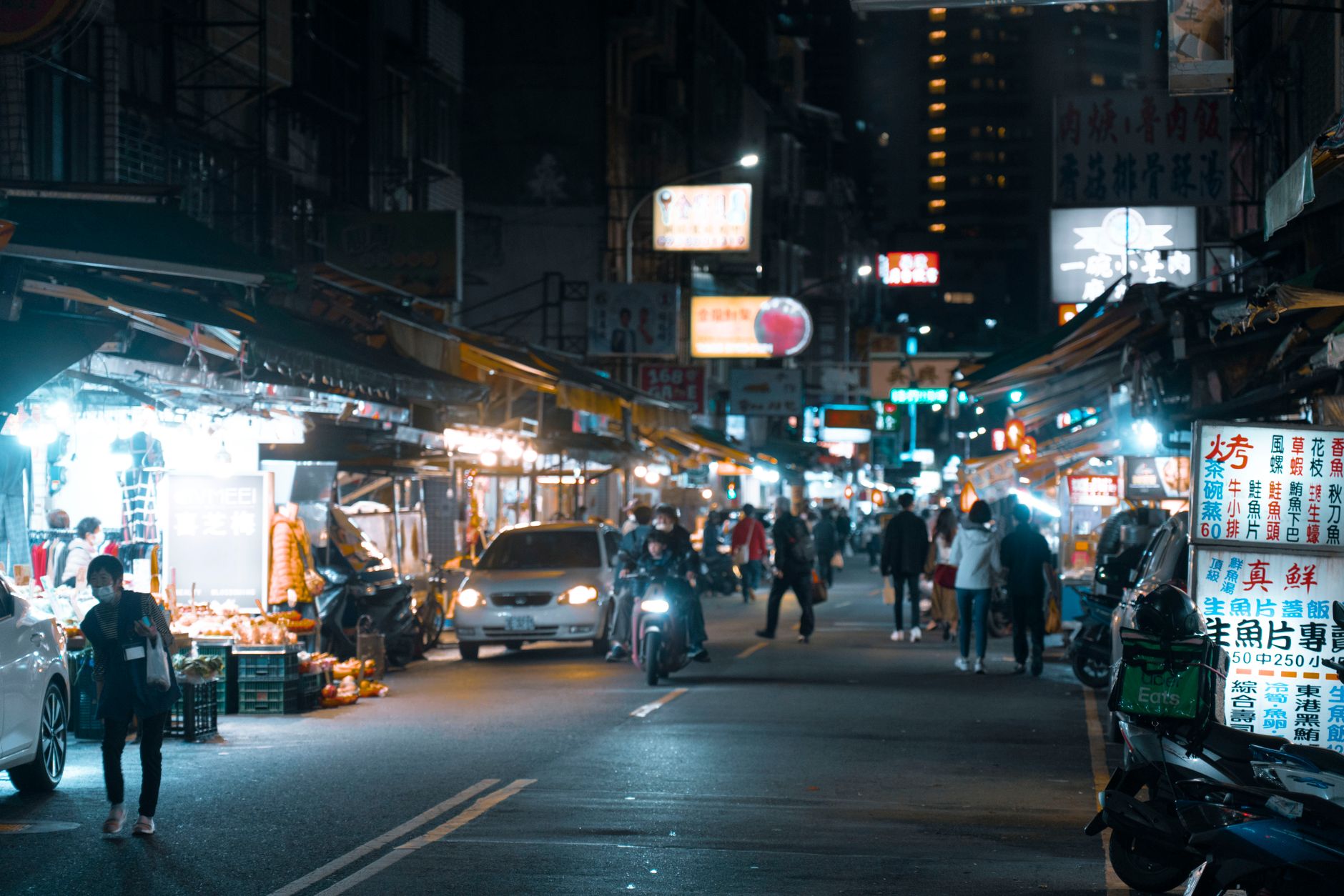 Shoppers walking between illuminated stalls at a night market after dark