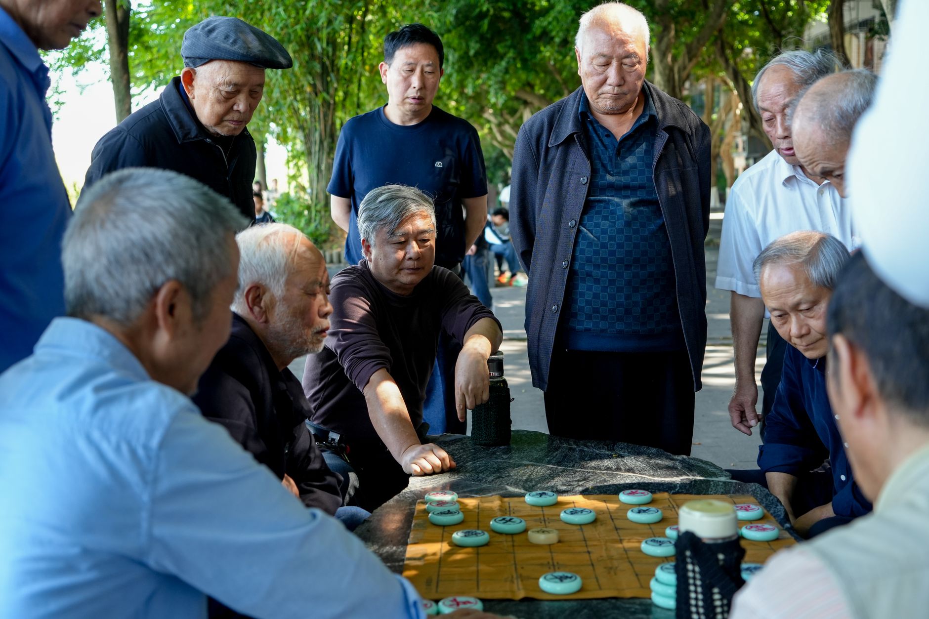 Older men gathered around an outdoor board of Chinese chess in a city park