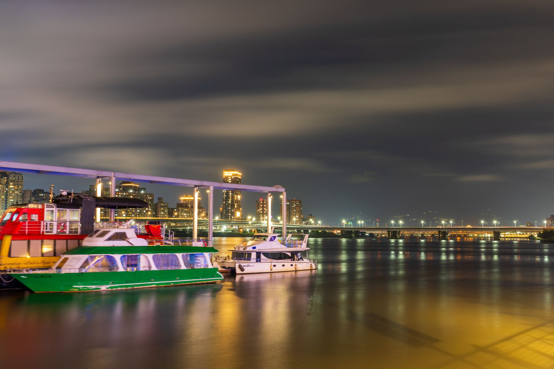 Sightseeing boats moored on the river below a lit-up waterfront