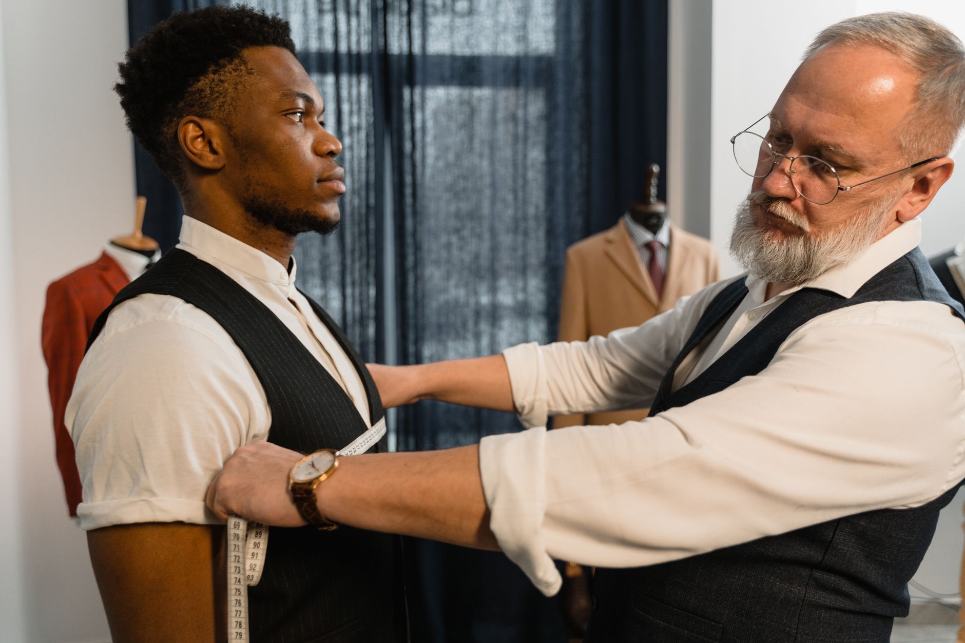 A tailor taking measurements for a bespoke suit fitting in a tailoring workshop
