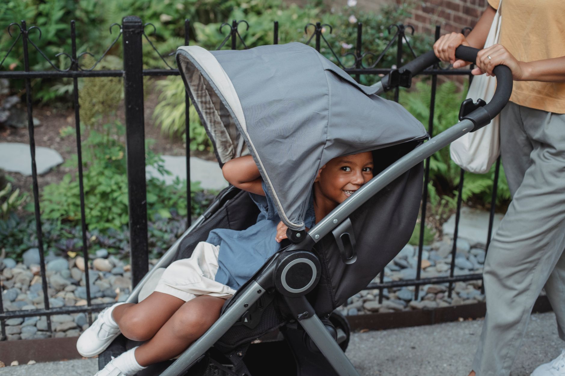 A toddler riding in a pushchair while a parent walks along a city pavement