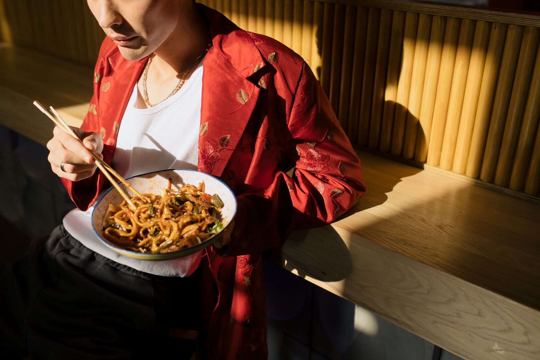 A solo diner eating a bowl of noodles with chopsticks at a bright Asian restaurant counter