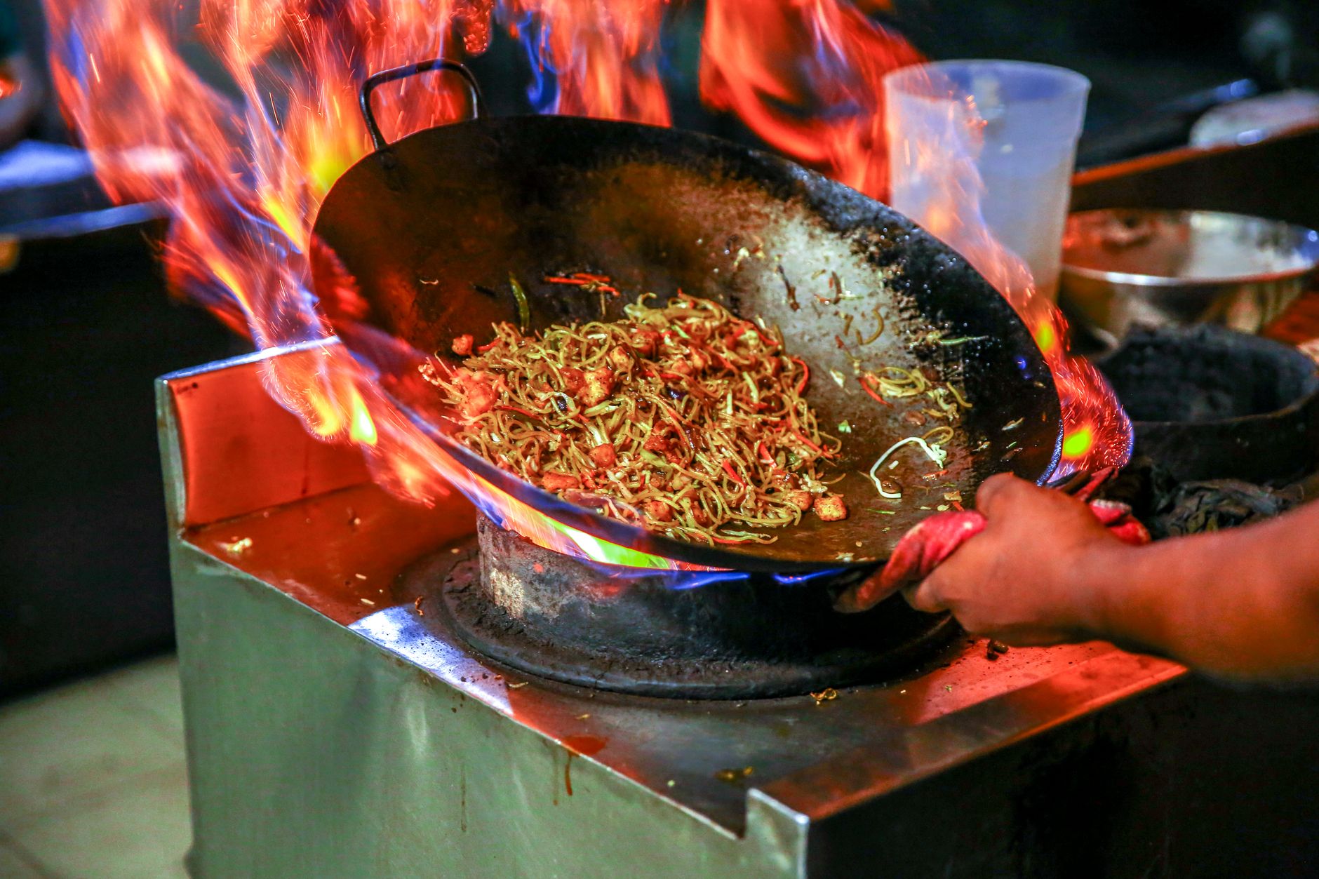 A cook tossing noodles in a wok over a high flame in a Chinese restaurant kitchen