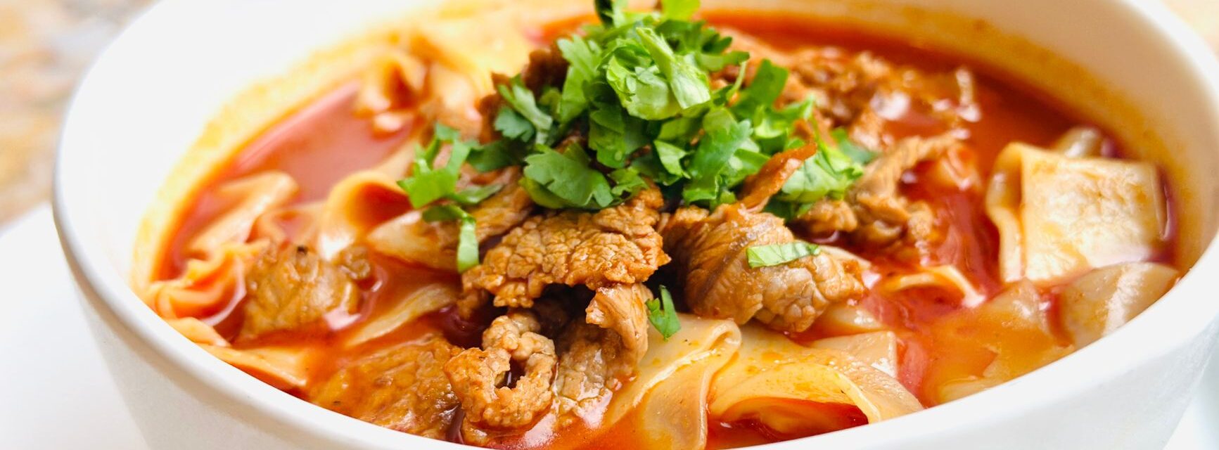 A bowl of beef noodle soup with hand-cut noodles and coriander