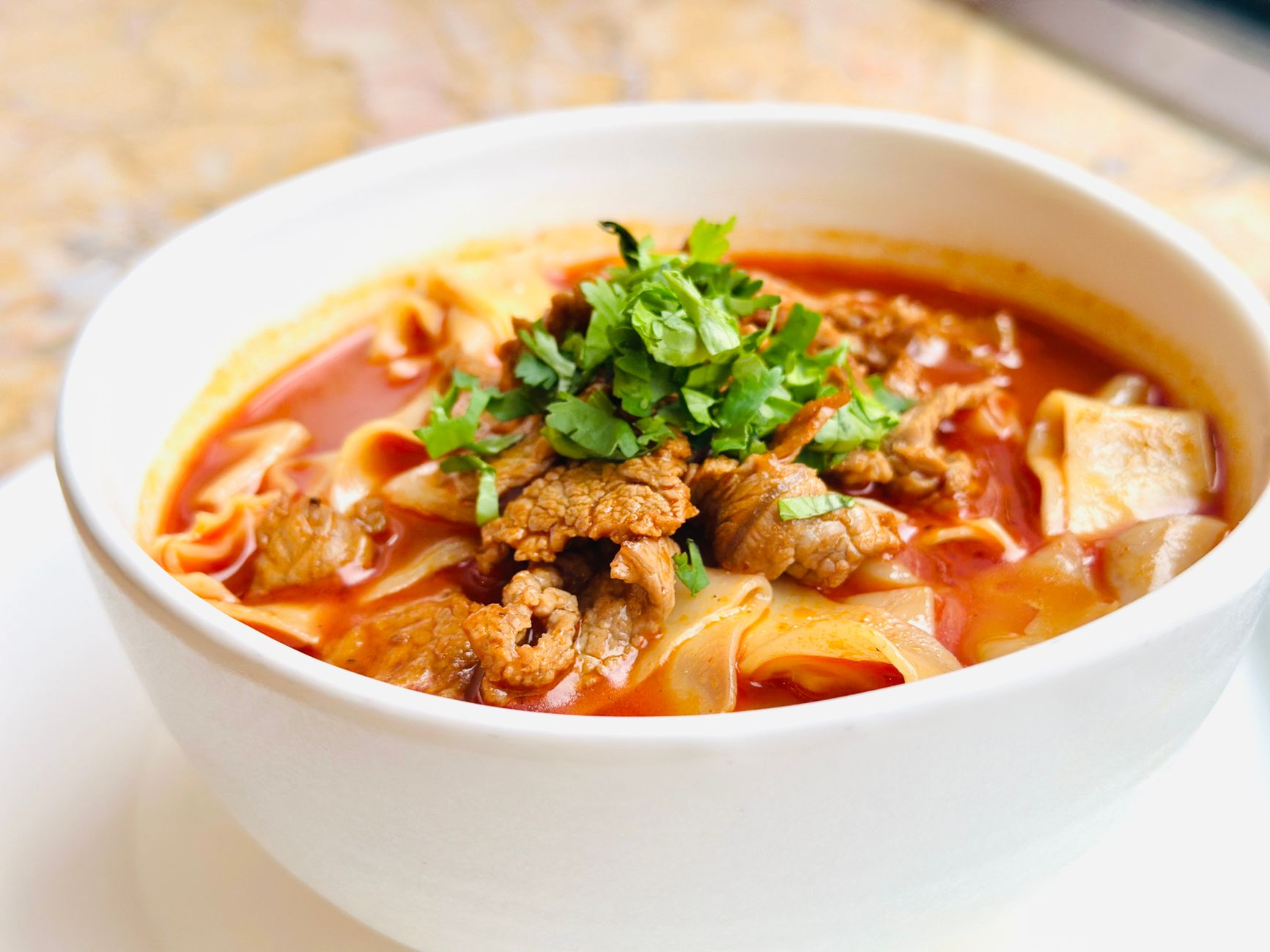 A bowl of beef noodle soup with hand-cut noodles and coriander