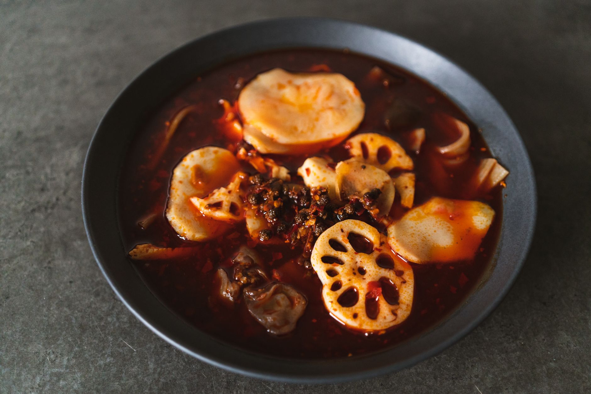 A bowl of spicy Sichuan-style hot pot with lotus root slices in red chilli broth