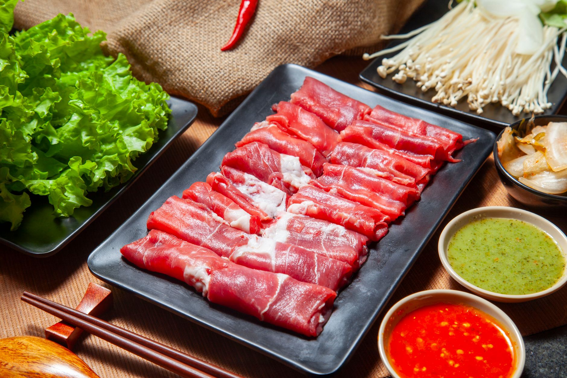 A platter of thinly sliced raw beef with lettuce, enoki mushrooms and dipping sauces