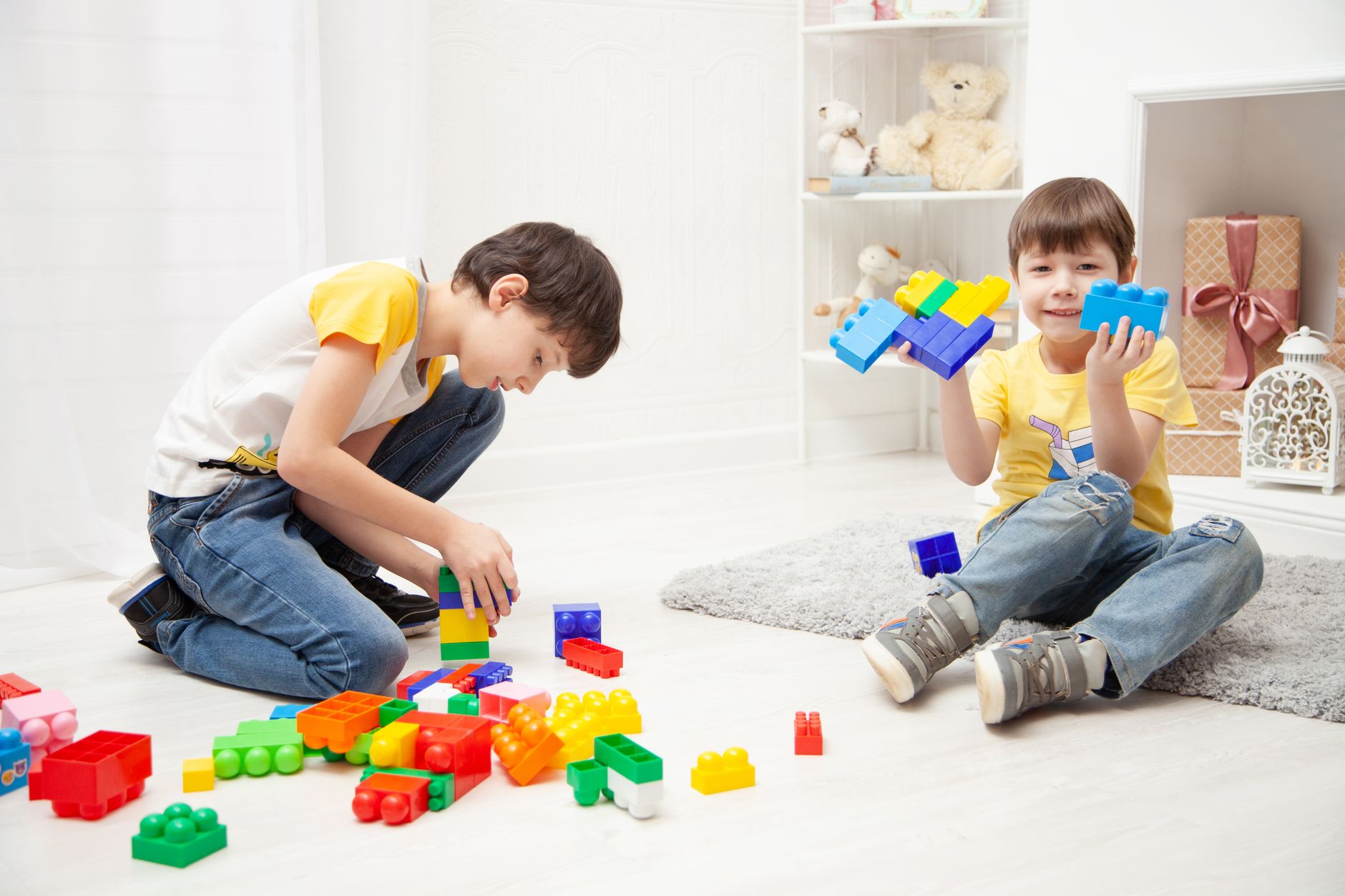 Two young children building with colourful plastic bricks on the floor