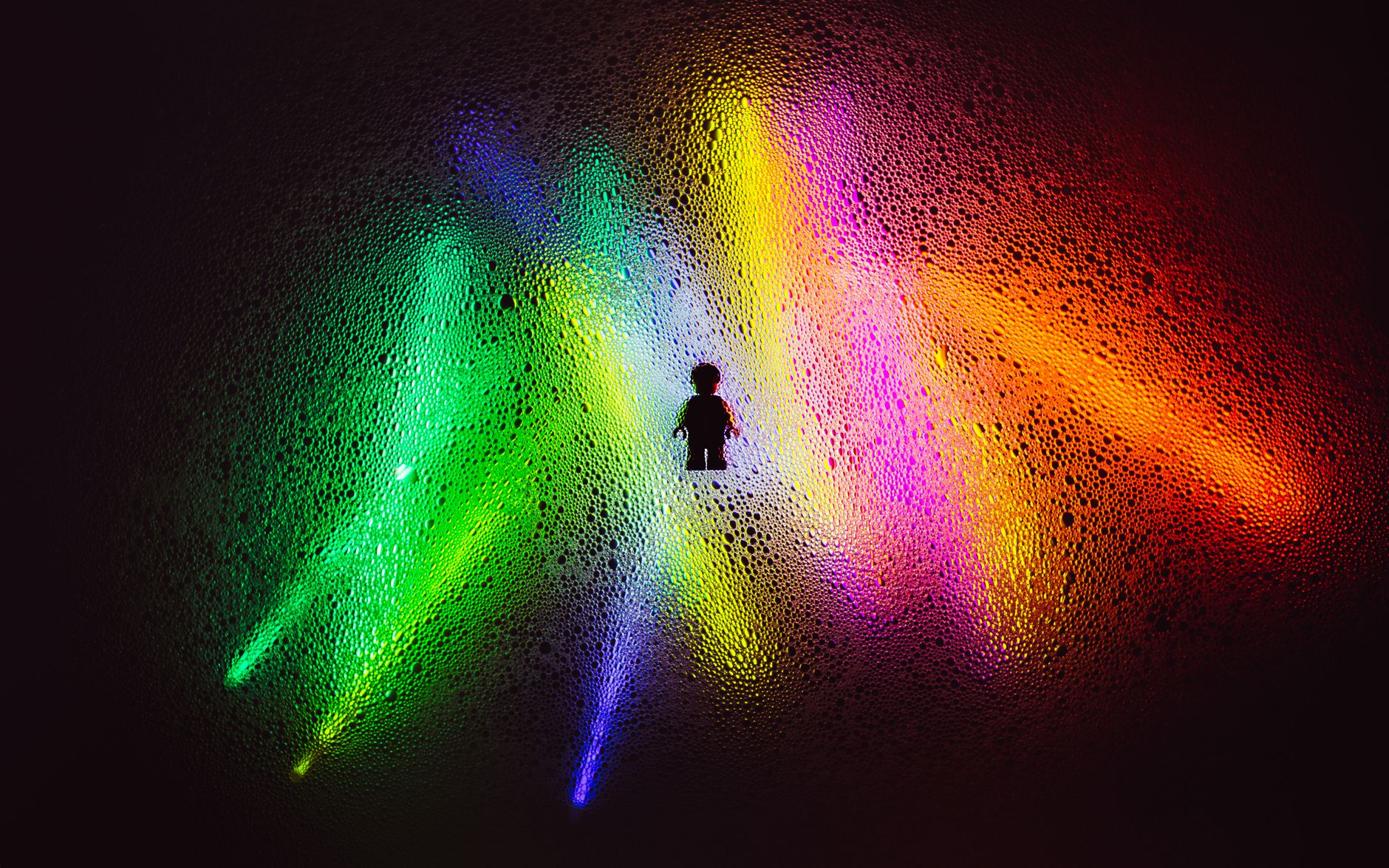 A single toy minifigure silhouetted against bands of coloured light