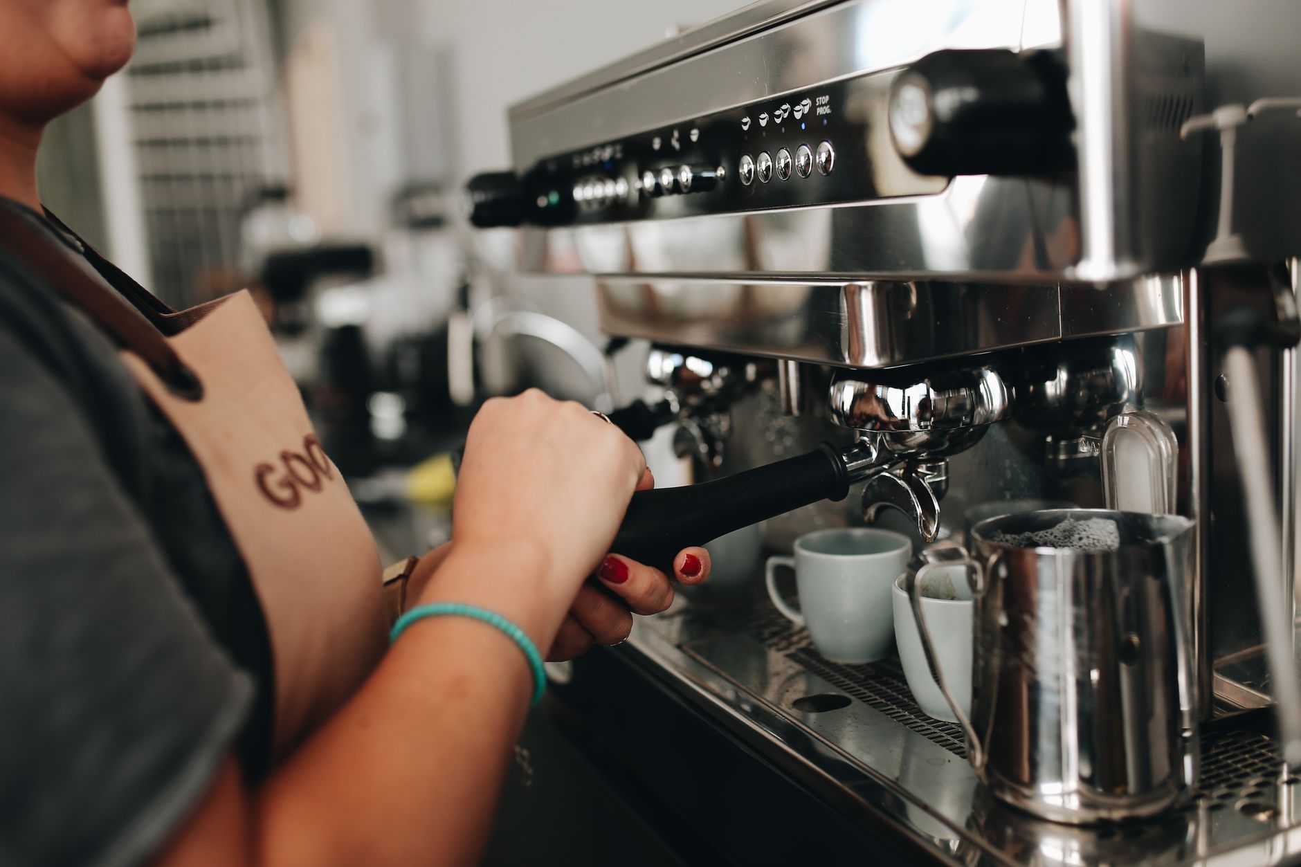 A barista fitting a portafilter into an espresso machine in a small café