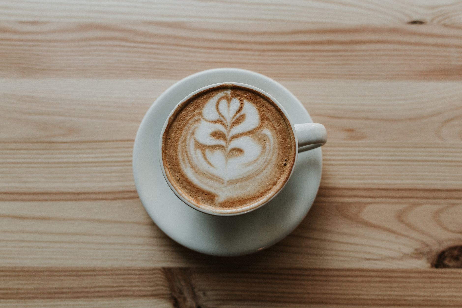 A flat white with leaf latte art in a white cup on a wooden table