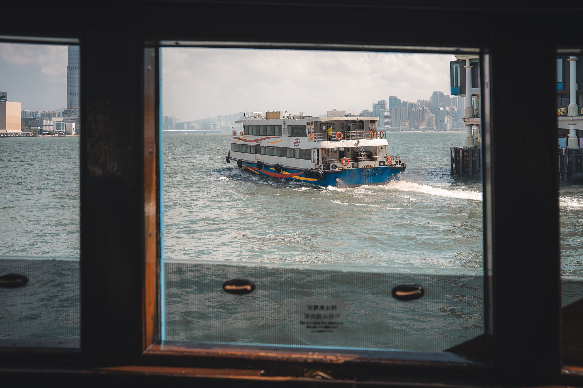 A harbour ferry crossing Victoria Harbour seen from inside a Hong Kong pier waiting hall