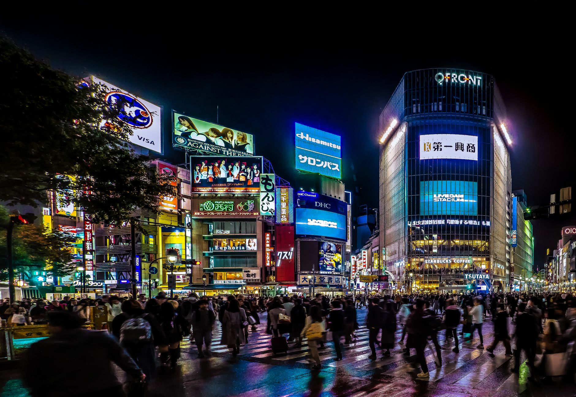 Crowds crossing Shibuya Crossing in Tokyo at night beneath illuminated billboards