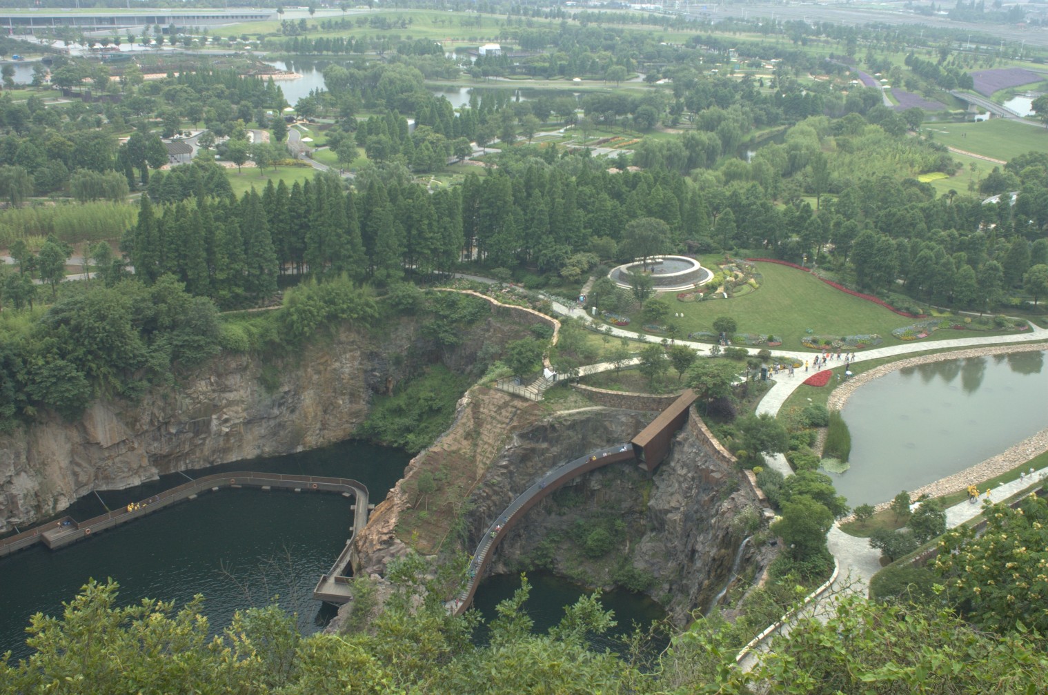 Aerial view of a former quarry turned into a garden, with a deep pool, cliffs, paths and green planting