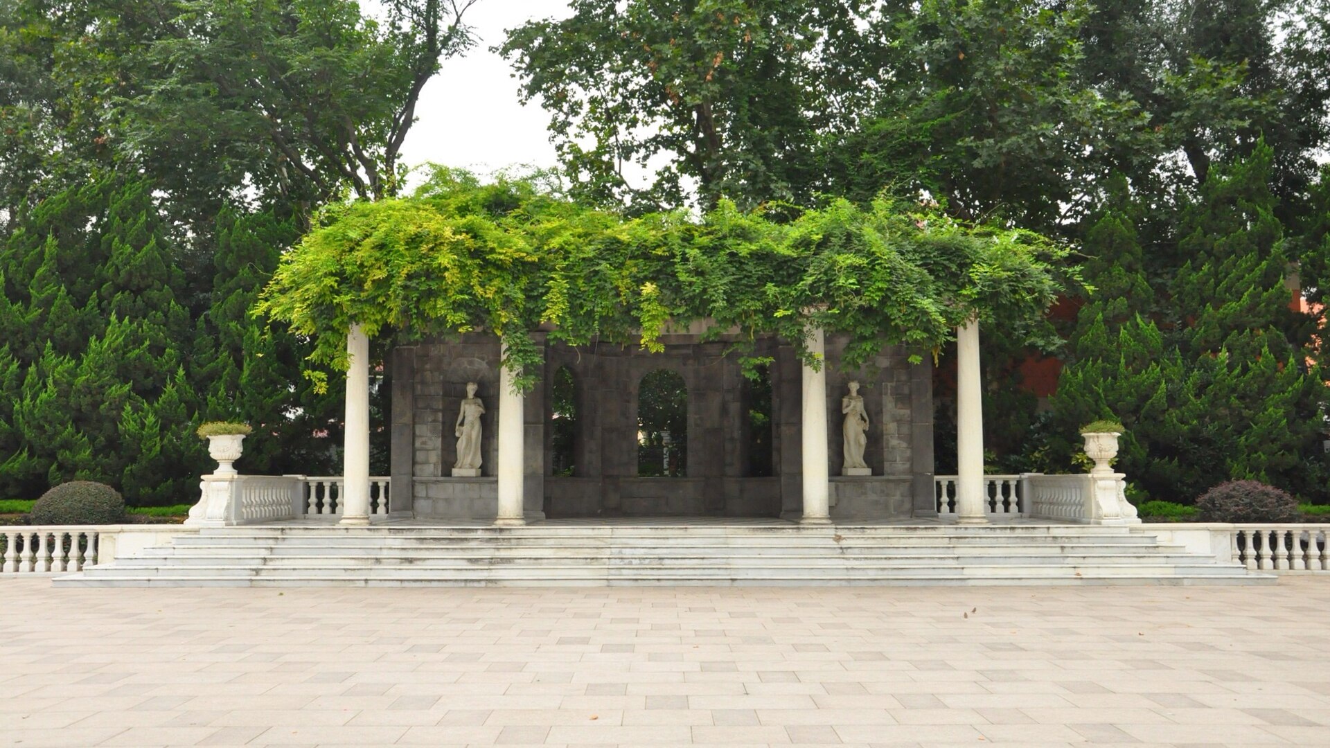 A white marble pavilion with columns and a vine-covered roof above stone steps in Zhongshan Park
