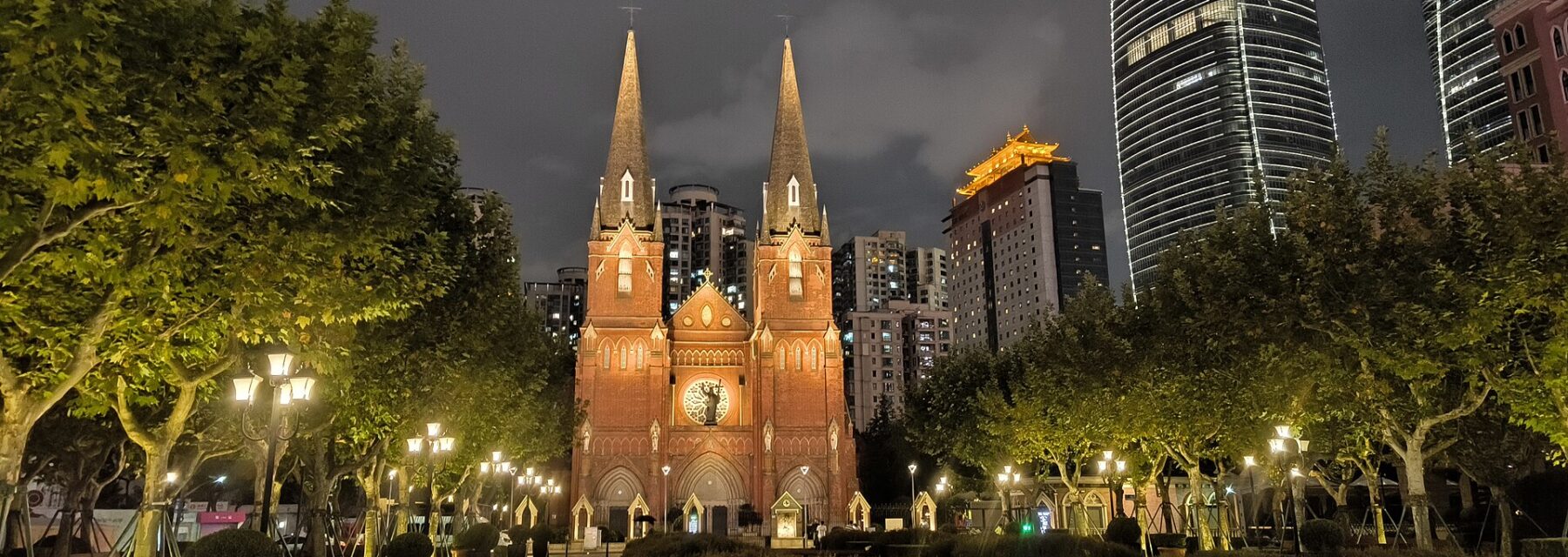 The twin spires of St Ignatius Cathedral in Xujiahui lit up at night, with tower blocks behind