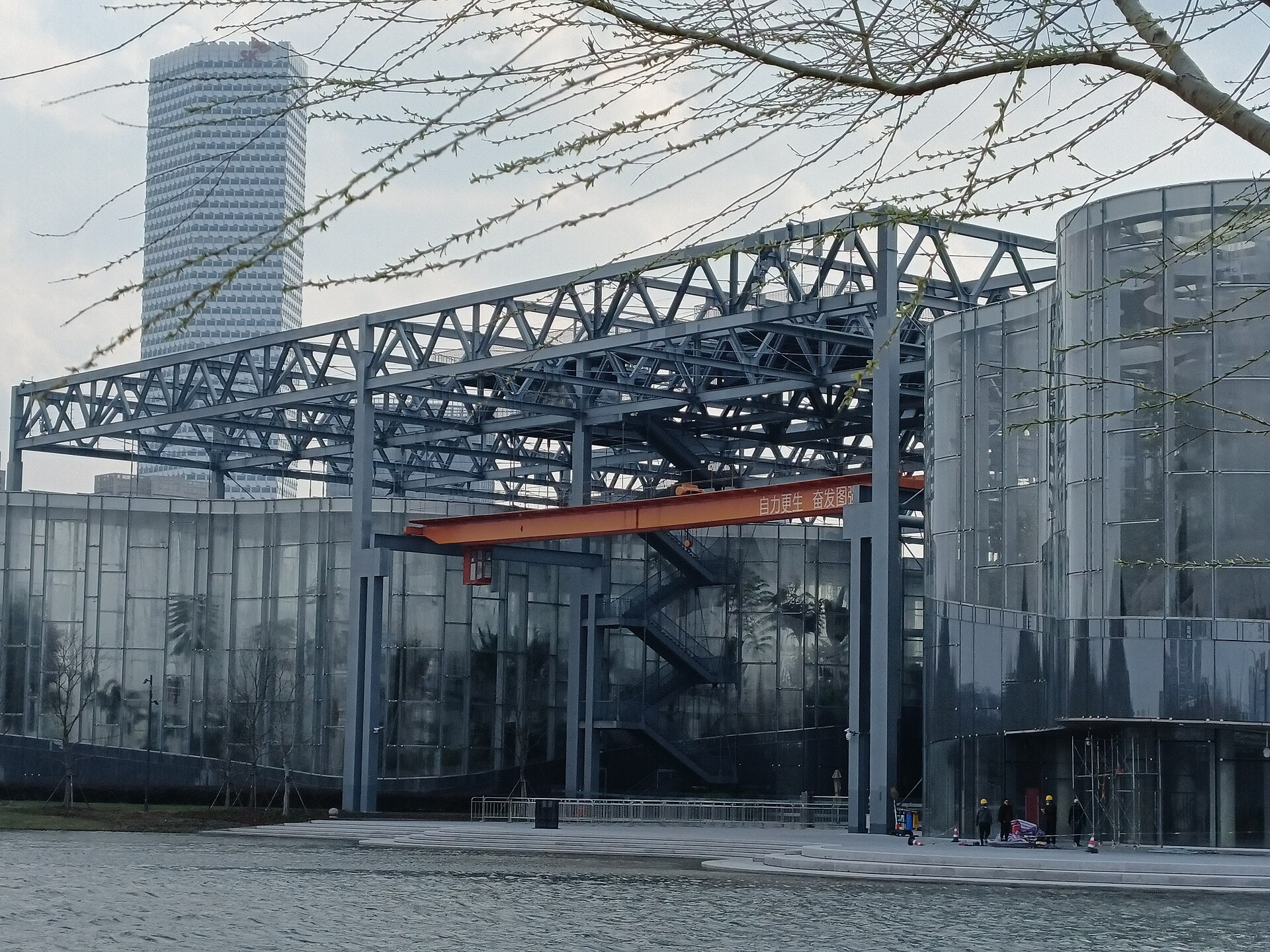 Curved glass walls shelter trees beneath an exposed industrial steel frame at Shanghai Greenhouse in Expo Culture Park.