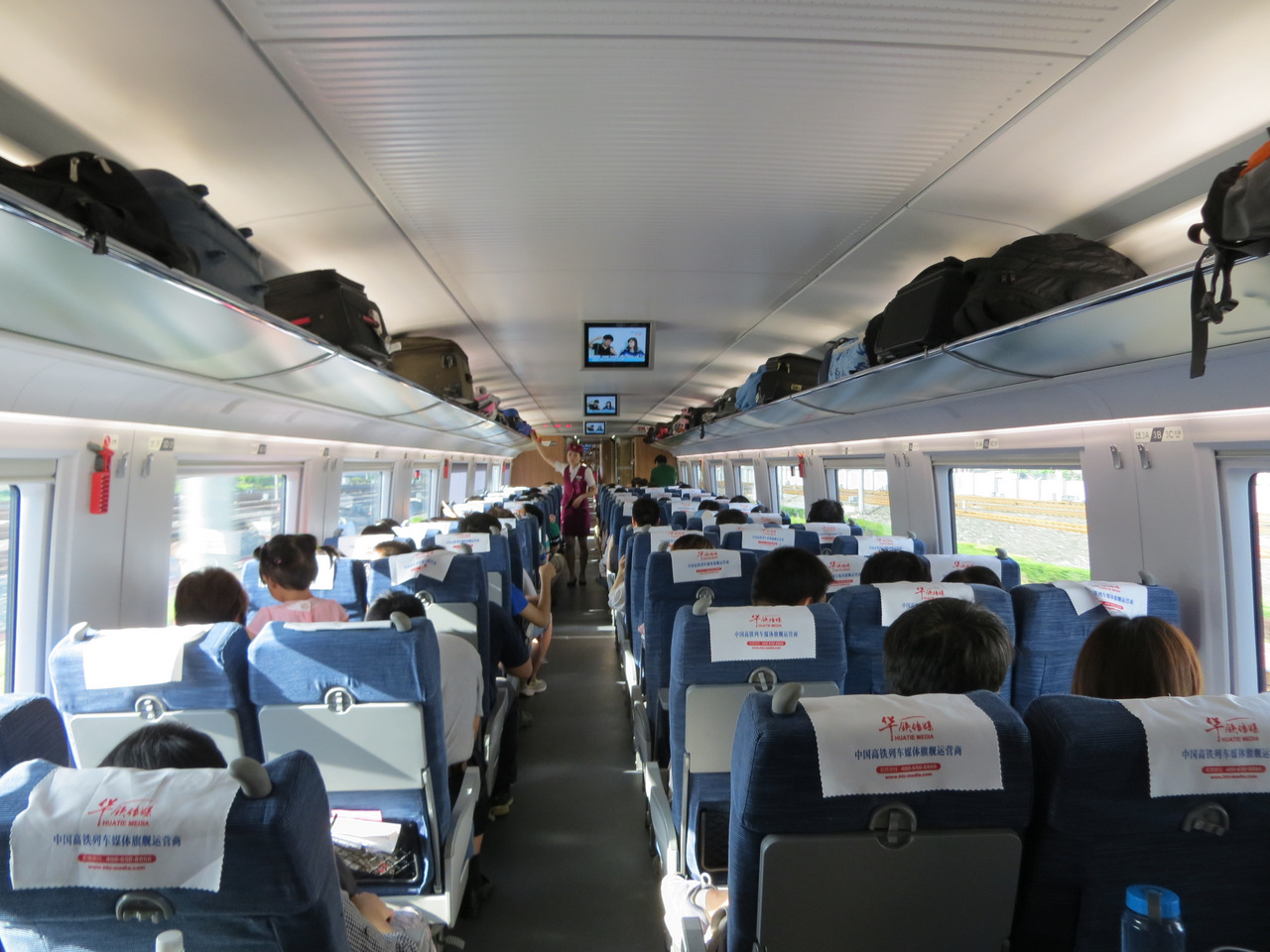 Passengers occupy blue three-plus-two seats beneath overhead luggage shelves inside a China Railway CRH3C second-class carriage.