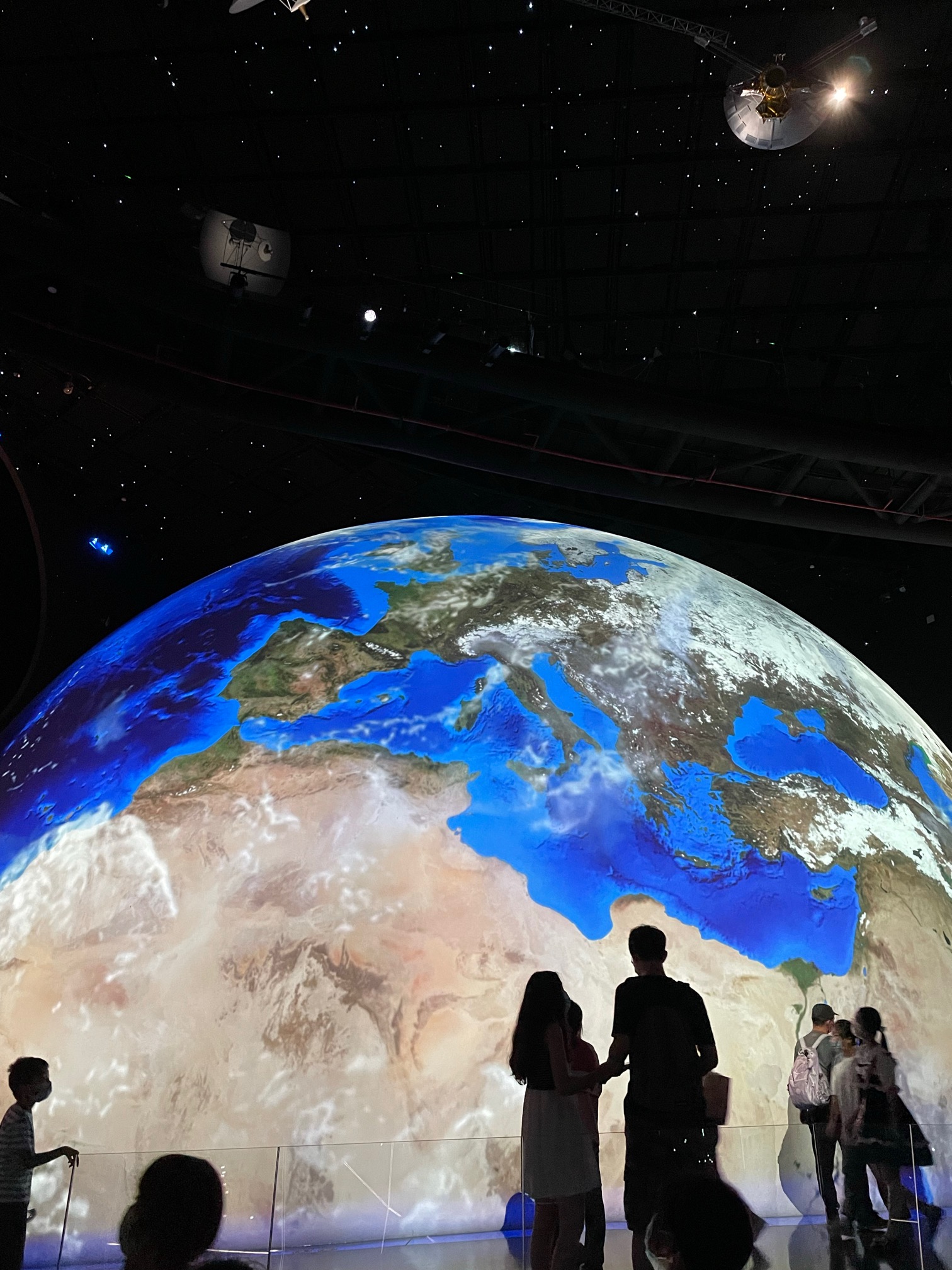 Visitors silhouetted against a huge projected model of the Earth hanging in a dark hall