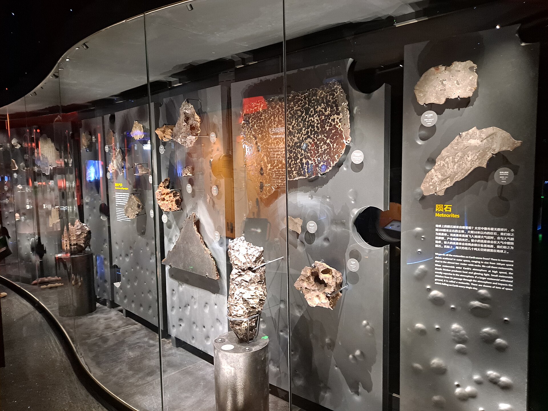 A wall of meteorite specimens in glass cases with information panels at the Shanghai Astronomy Museum