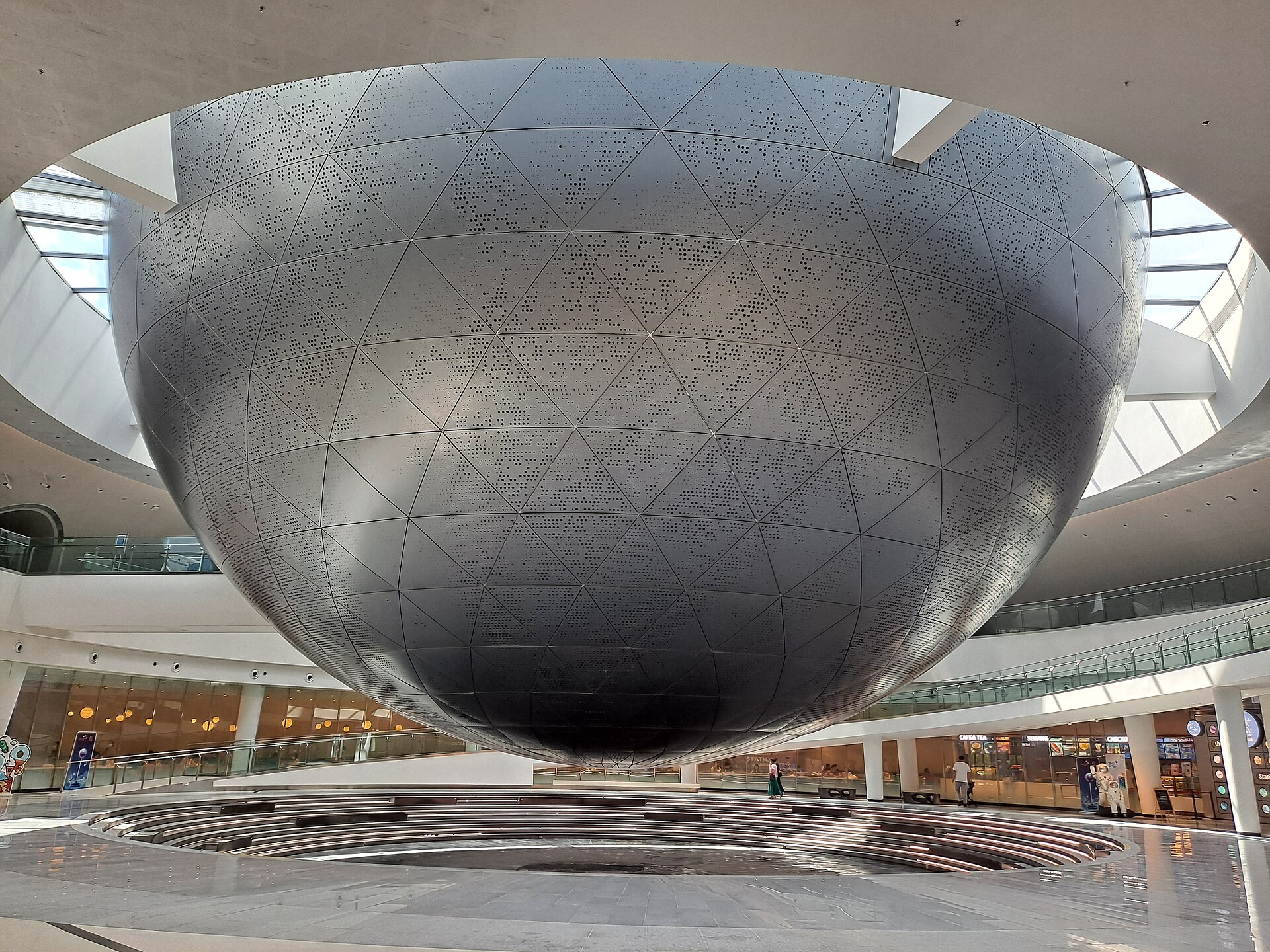 A huge silver sphere with a perforated metal skin suspended over a curved white atrium inside the Shanghai Astronomy Museum