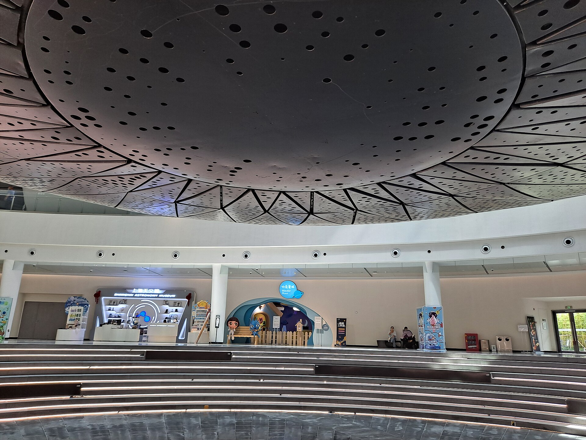 Looking up at the underside of a giant perforated sphere above a curved atrium with tiered seating below