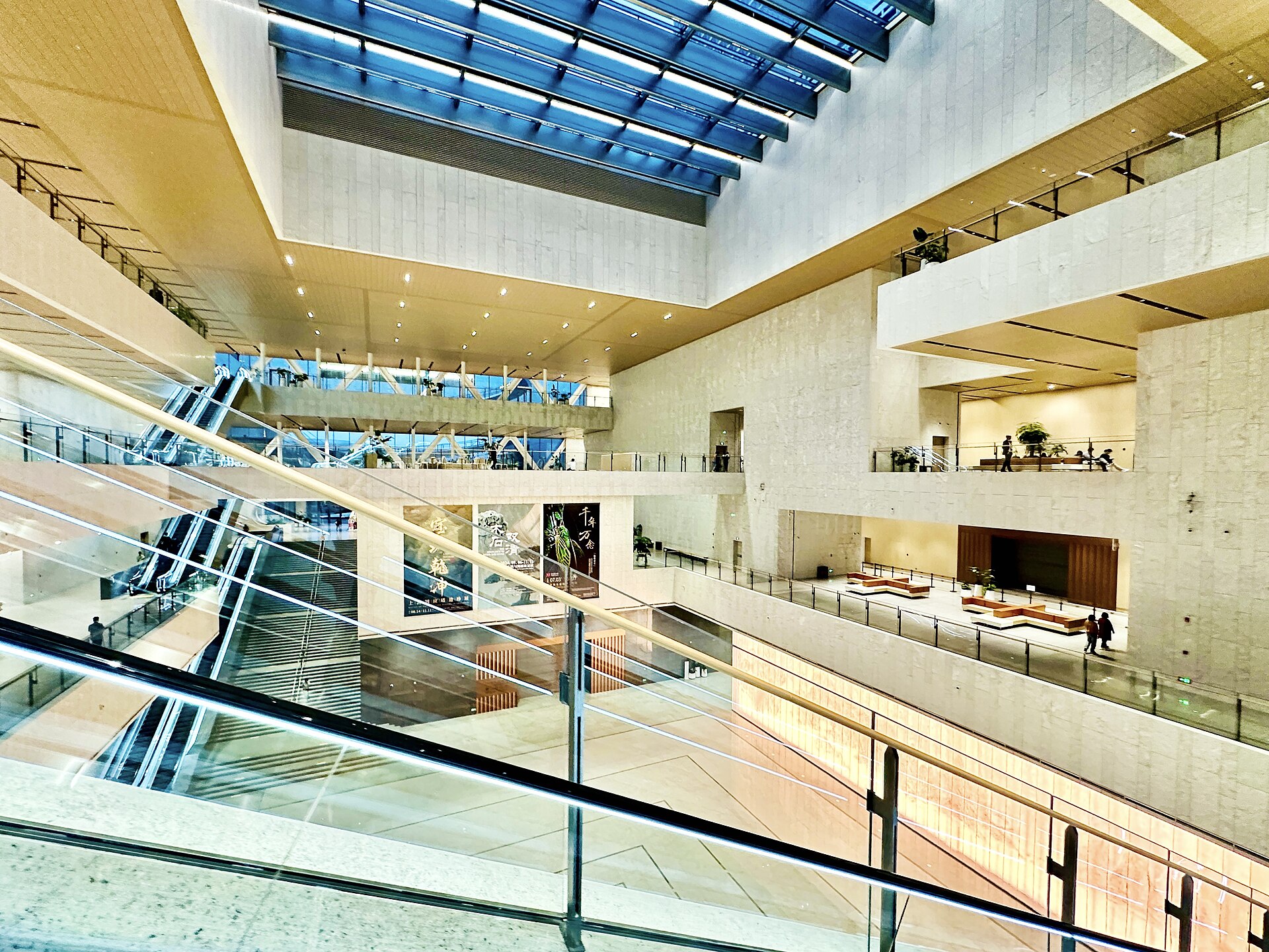 A tall white atrium inside Shanghai Museum East with escalators, glass balustrades and a glazed roof