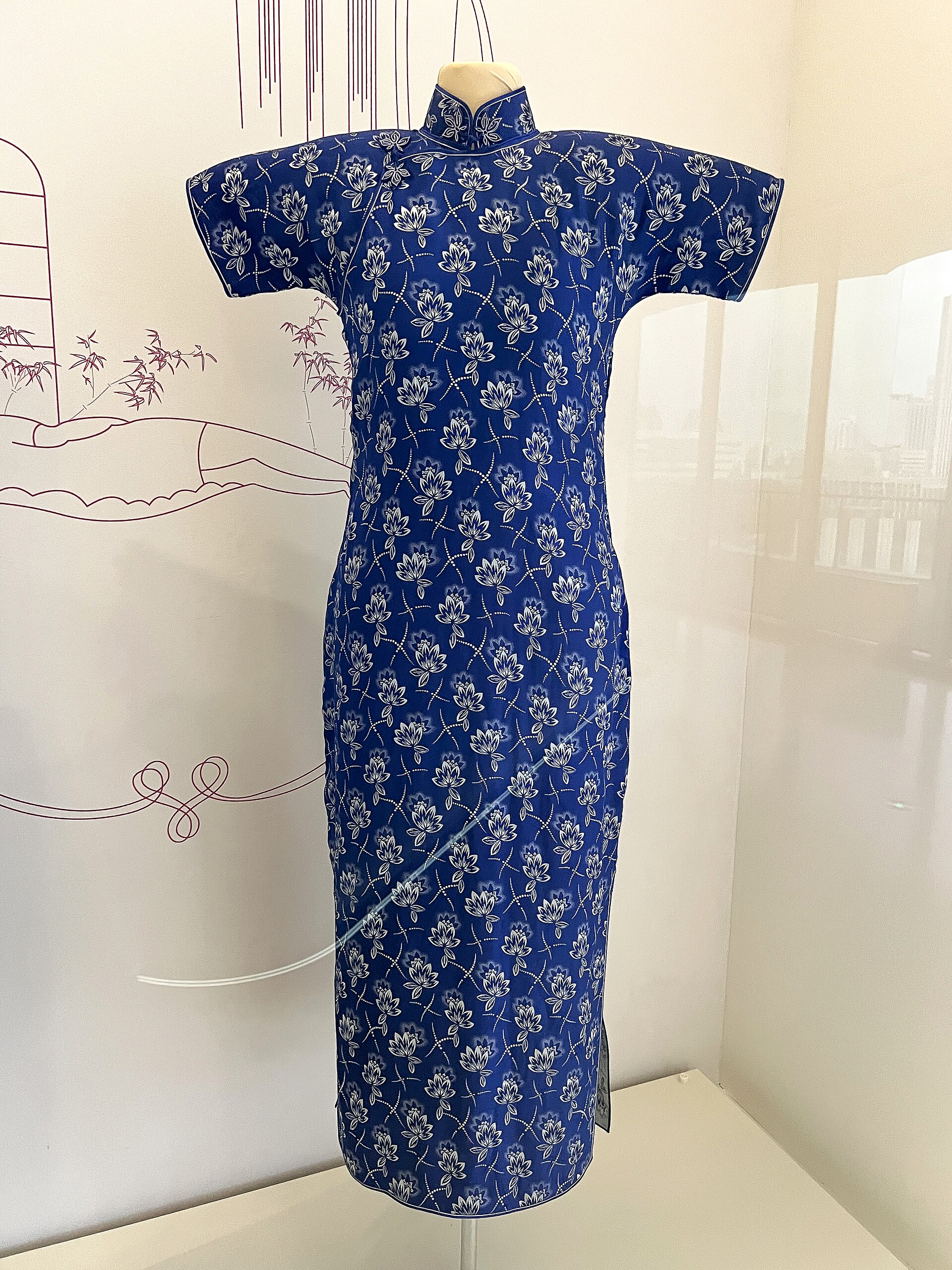 A 1930s blue qipao with a silver and white floral pattern displayed on a mannequin