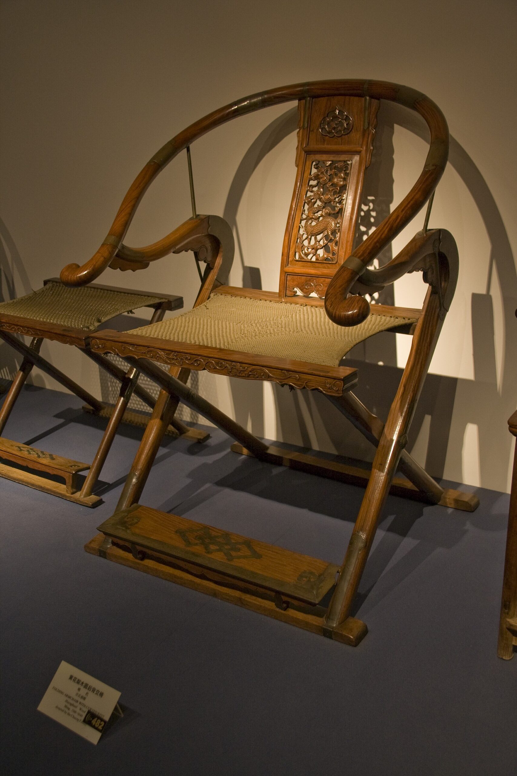 A carved wooden folding armchair with a curved horseshoe back in a museum display