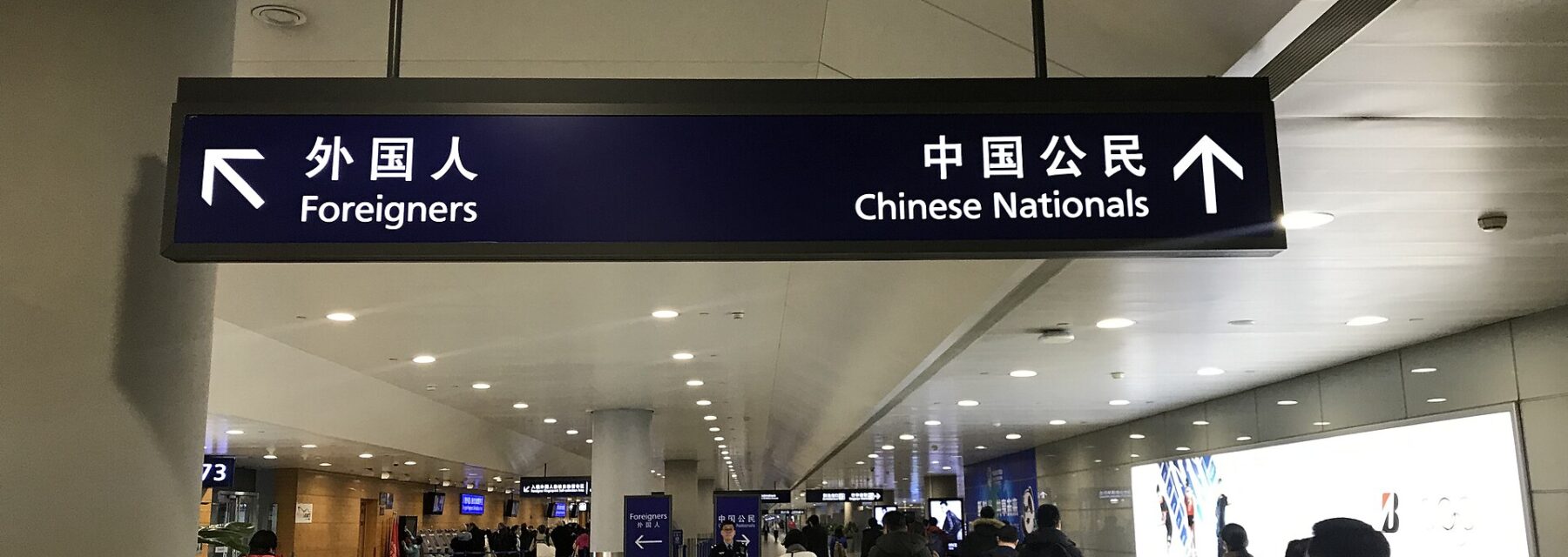 Travelers approach immigration at Shanghai Pudong Airport beneath bilingual signs directing foreigners and Chinese nationals to separate lanes.